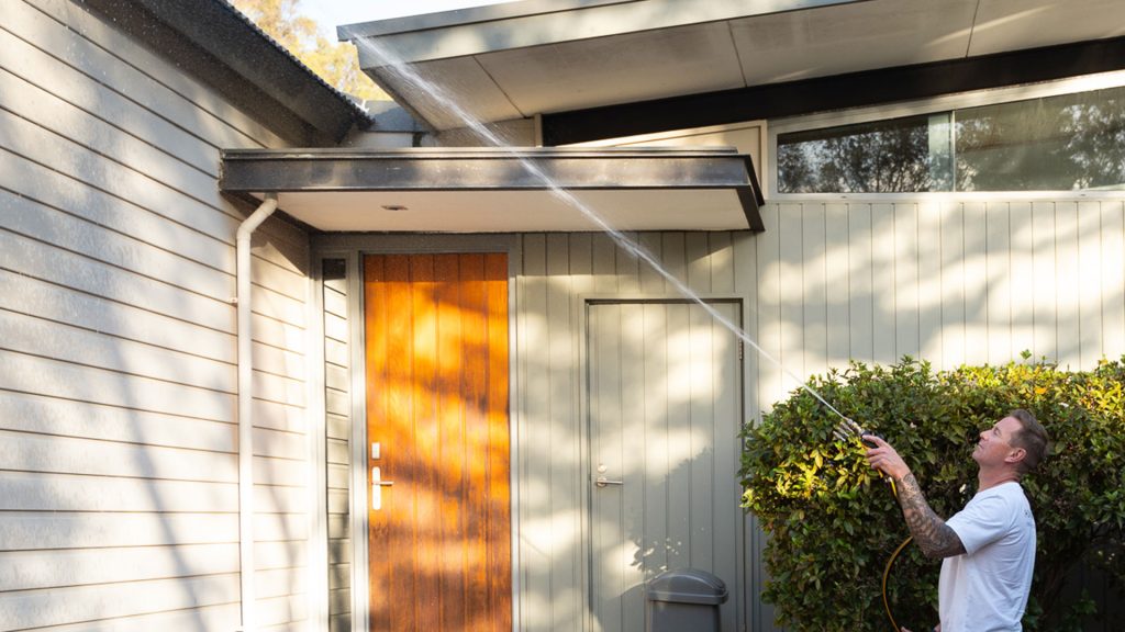 Professional cleaner using a pressure washer to clean gutters on a modern residential property.
