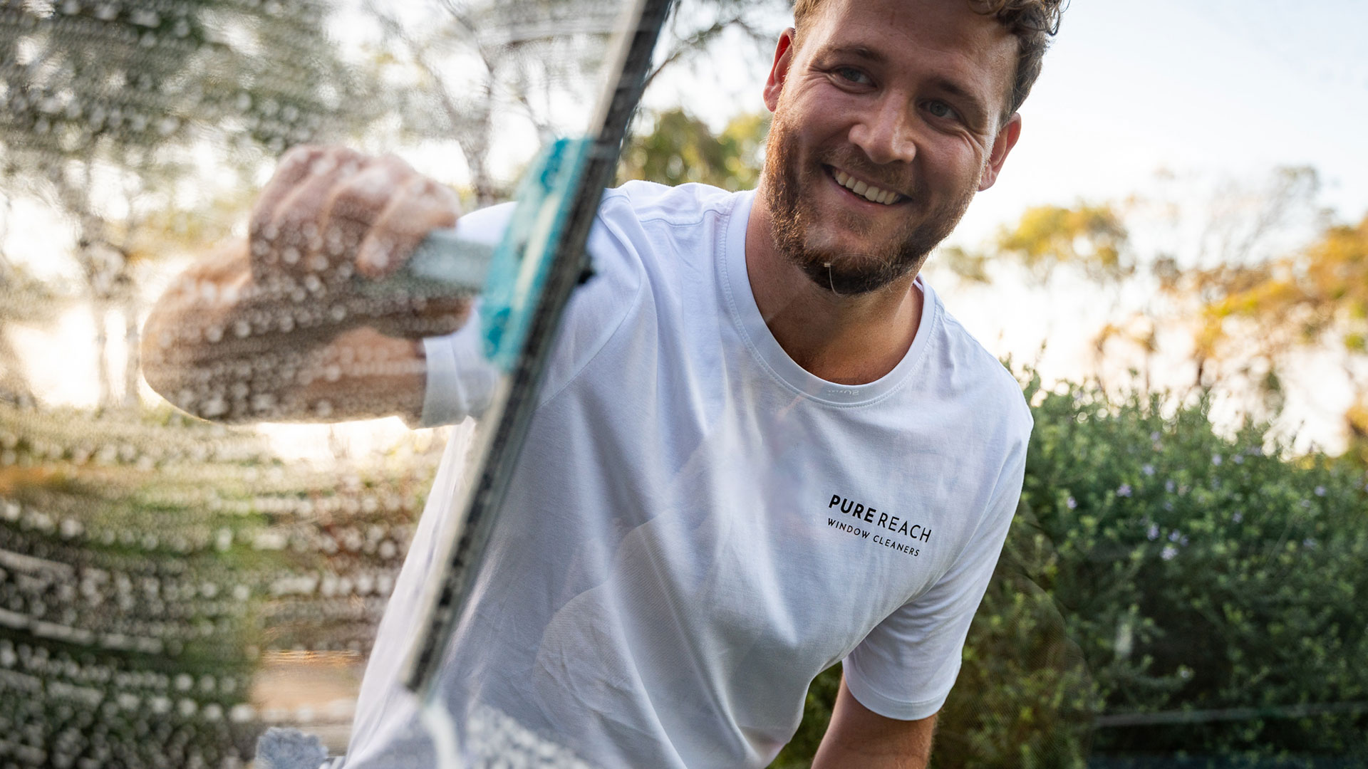 Friendly window cleaner providing residential cleaning services, ensuring spotless and streak-free windows in a serene outdoor setting.