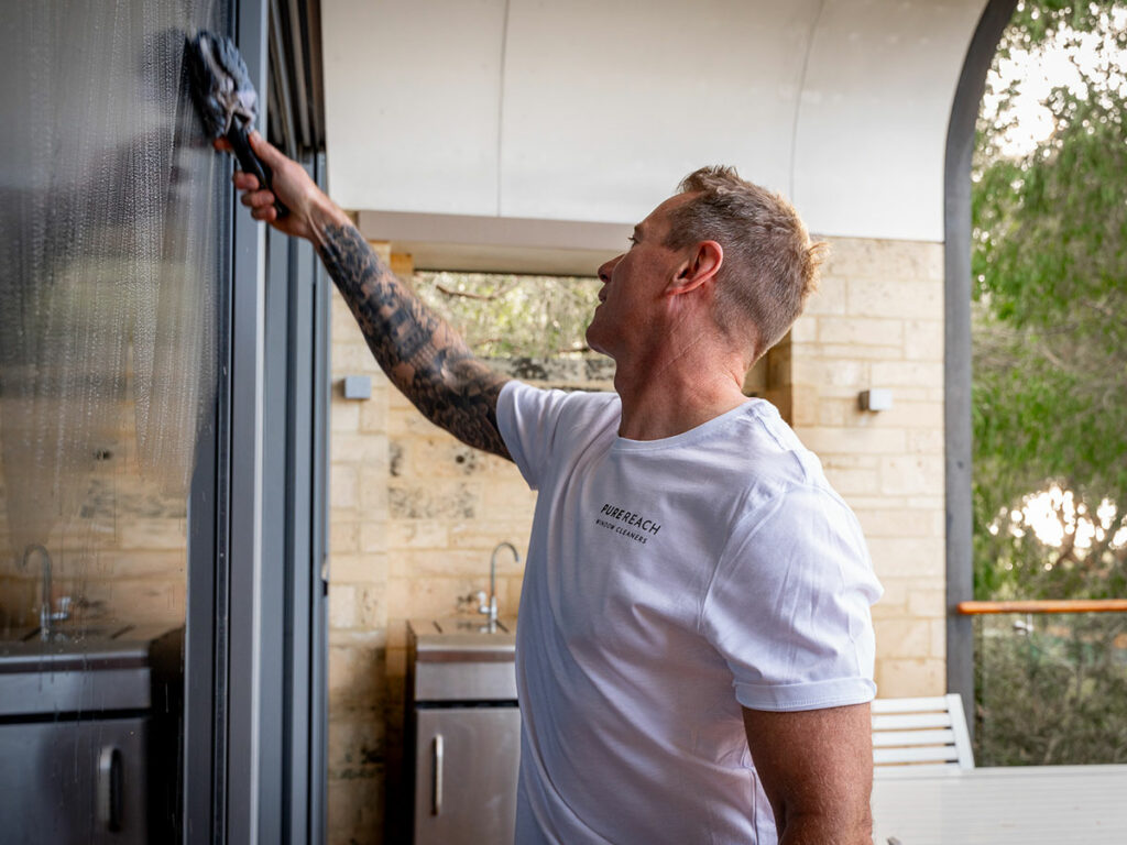 Residential cleaner in Margaret River expertly washing a glass door with a microfibre mop, delivering spotless results for a home.