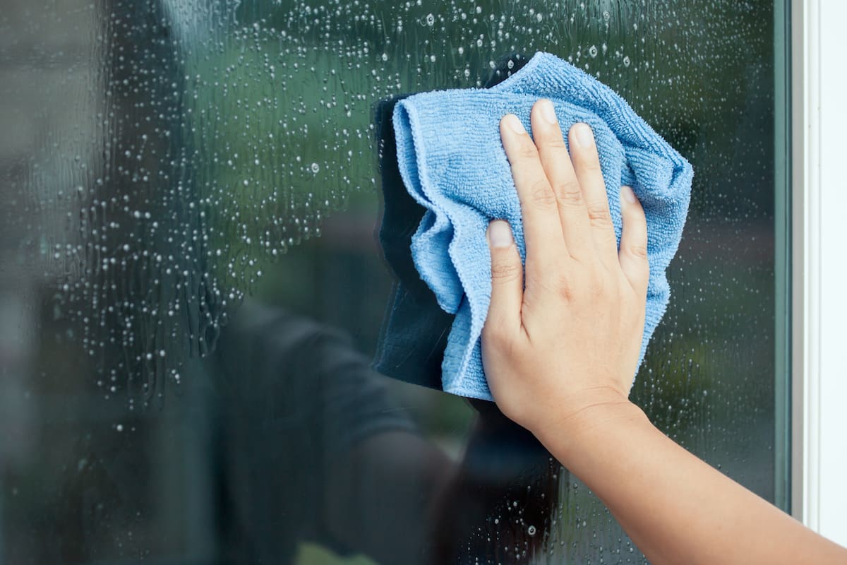 Hand wiping a wet tinted window with a blue microfibre cloth during cleaning.