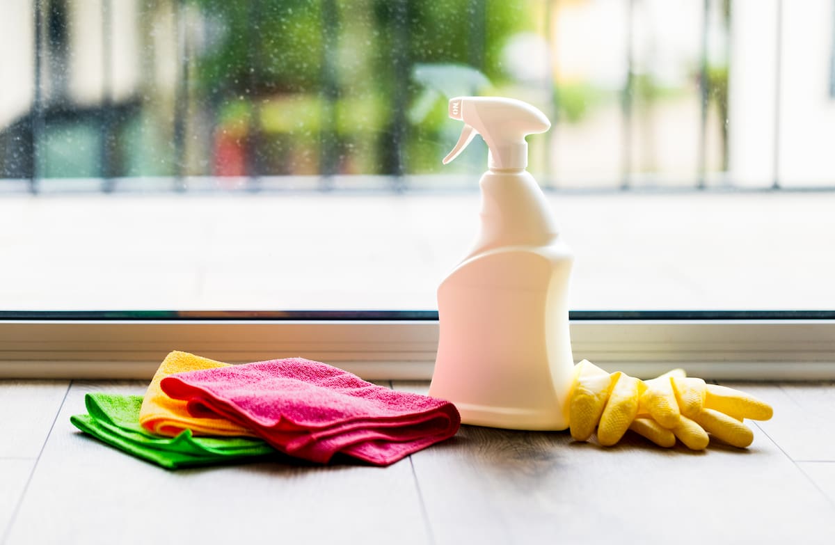Microfibre cloths, cleaning spray bottle, and gloves placed in front of a glass window, ready for cleaning.